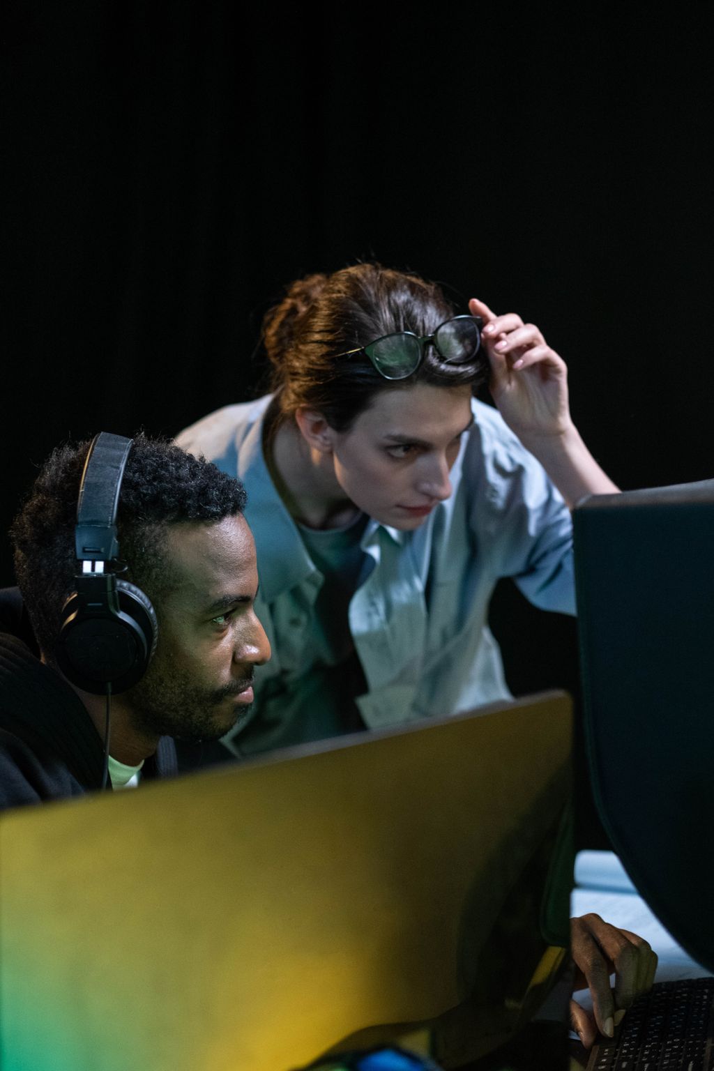 Two colleagues focusing on a post production video editing task in a dark studio environment.